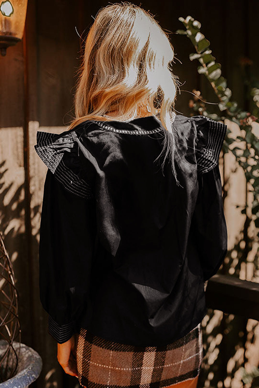 Blusa negra de manga larga con volantes, cuello en V y detalle de costura en contraste