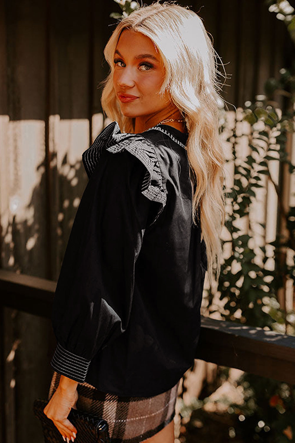 Blusa negra de manga larga con volantes, cuello en V y detalle de costura en contraste